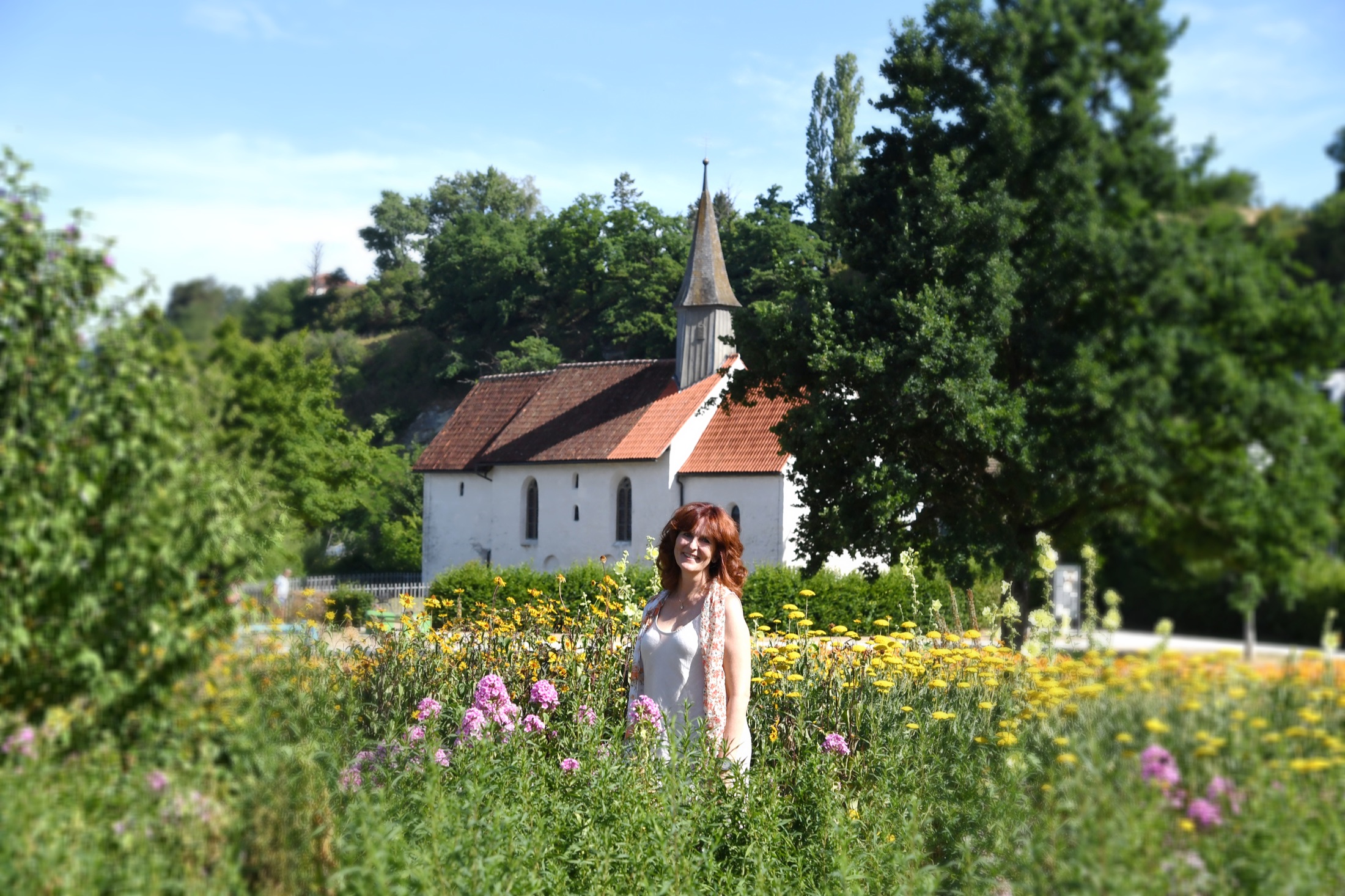 Sabine Heyer-Jahn steht in einer blühenden Sommerwiese vor einer kleinen weißen Kirche