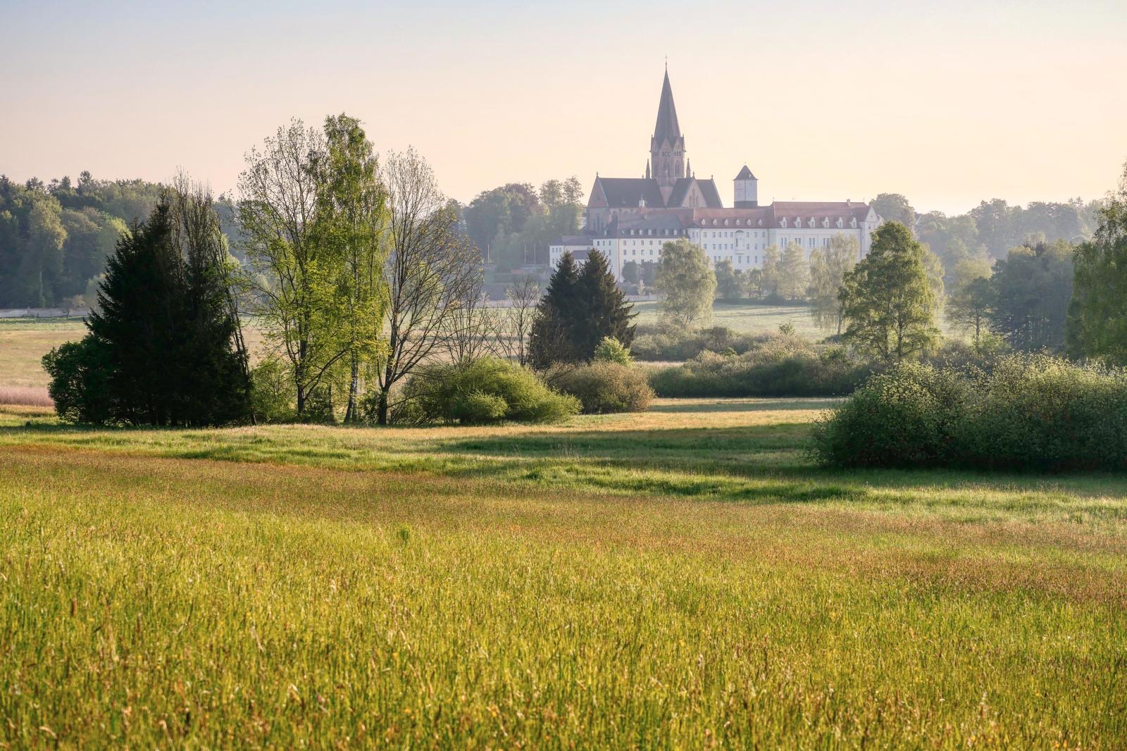 Die Erzabtei St. Ottilien im Morgenlicht hinter Wiesen und Bäumen