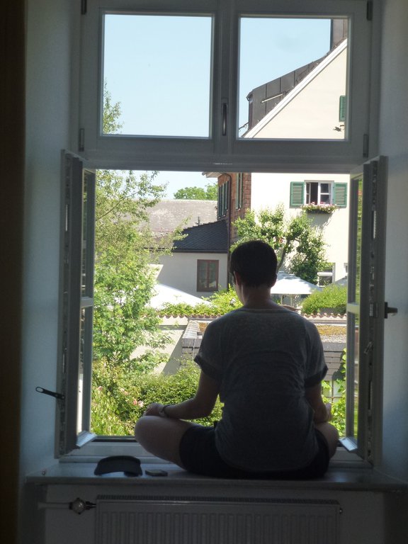 Eine Teilnehmerin sitzt meditierend im offenen Fenster und blickt auf die Dächer der Insel